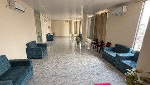 A hotel lobby with marble flooring, blue sofas, red chairs, and potted plants.