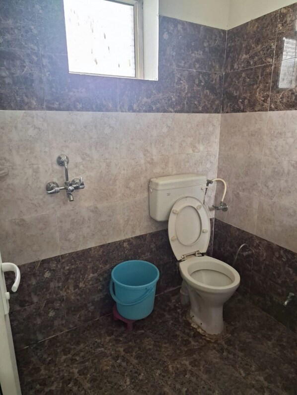 A bathroom with a toilet, a bidet, a window, and a blue bucket.