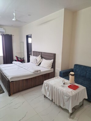 A hotel room with a bed, a small table with a red tray, a blue sofa, and a ceiling fan. - Sundervan Resort (Alwar)