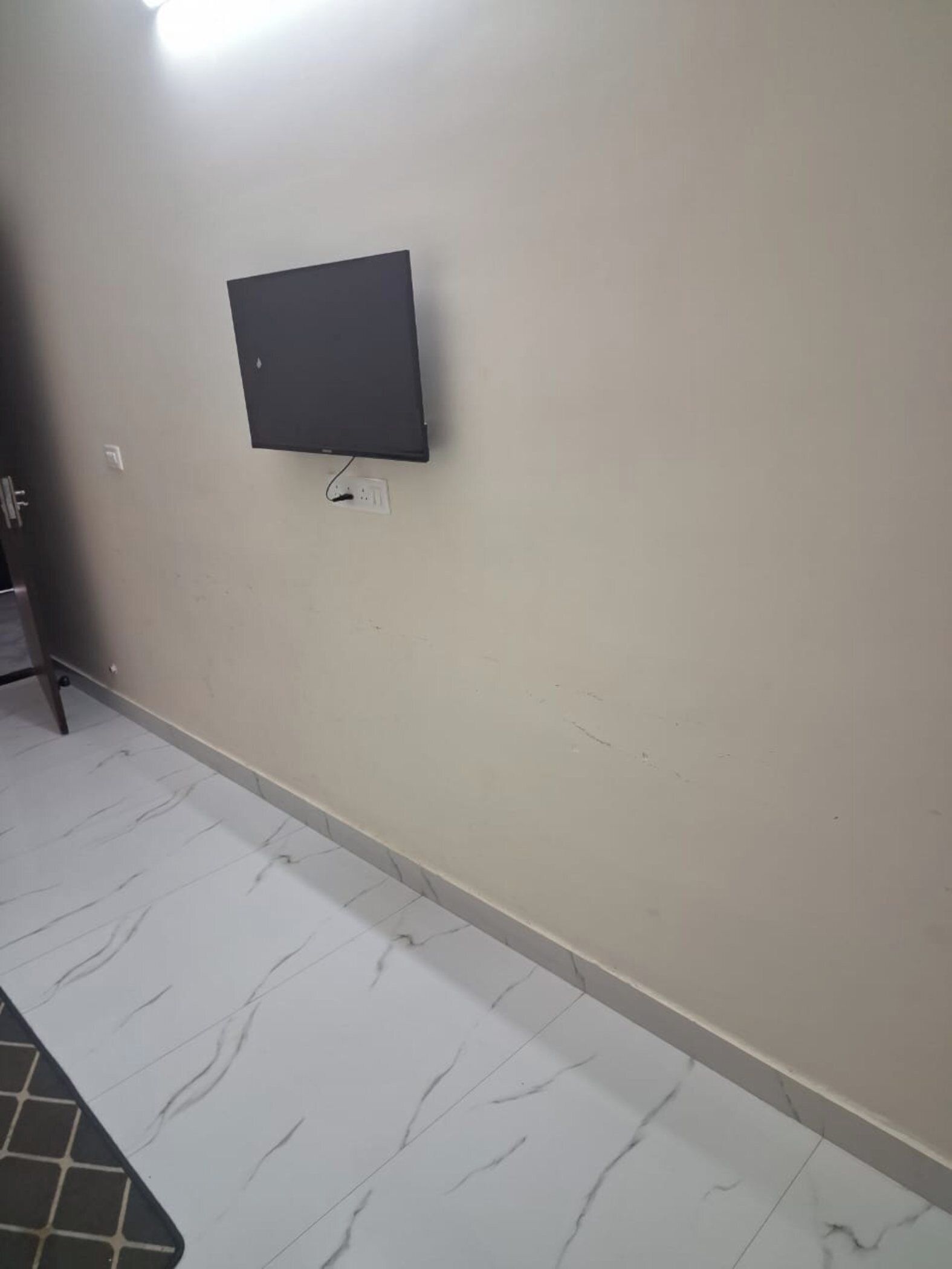 A room with a flat-screen TV mounted on the wall, a tiled floor, and a door on the left.