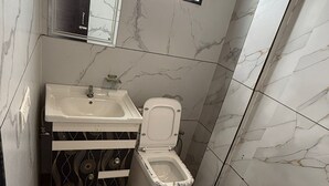 A bathroom with a white sink, toilet, and a window with a fan.
