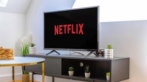 Moderni olohuone, jossa on seinälle asennettu taulutelevisio, jossa näkyy Netflix, pieni pyöreä pöytä, sohva ja koristeellisia kasveja.