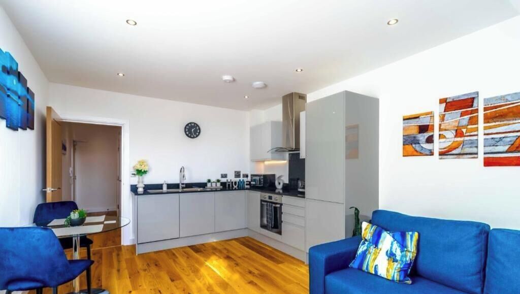Una cocina moderna con armarios blancos, una zona de comedor con un sofá azul y un reloj en la pared.