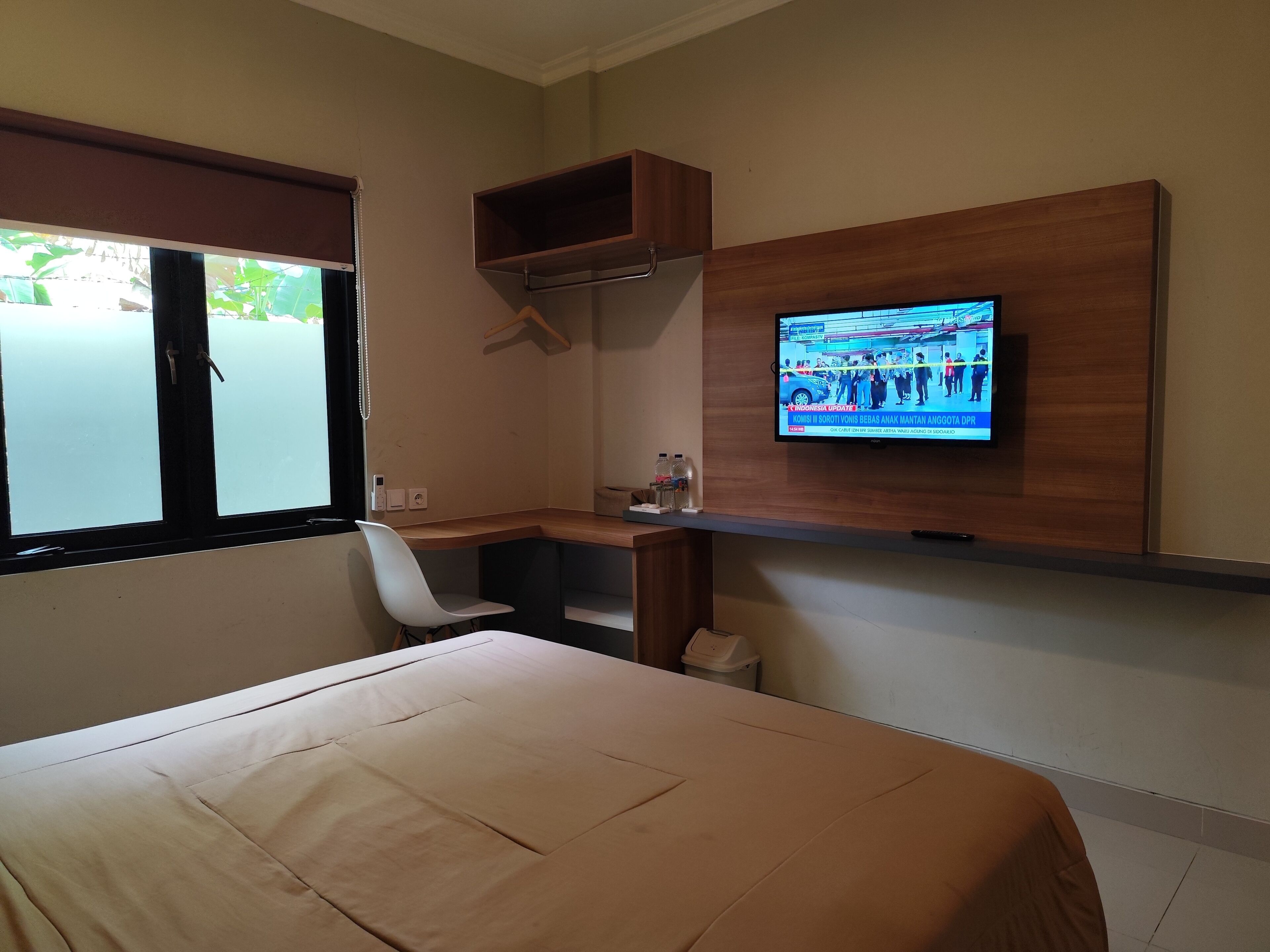 Ein Hotelzimmer mit Bett, Schreibtisch, Stuhl, an der Wand montiertem Fernseher und einem Fenster mit Jalousien.