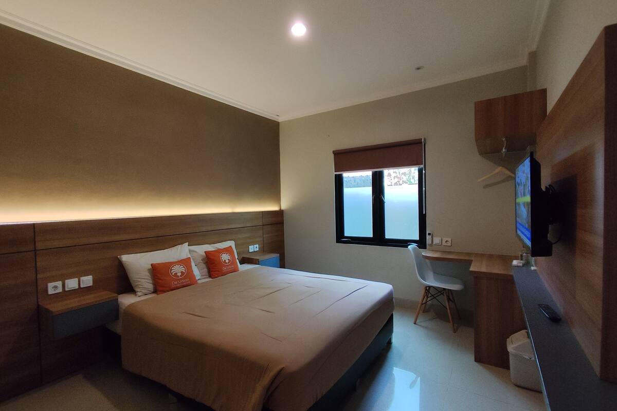 Un dormitorio con cama, mesitas de noche, escritorio, silla, televisor y ventana.