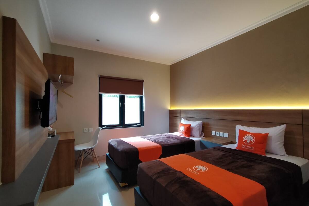 Habitación de hotel con dos camas, un escritorio, una silla, un televisor y una ventana con persianas.