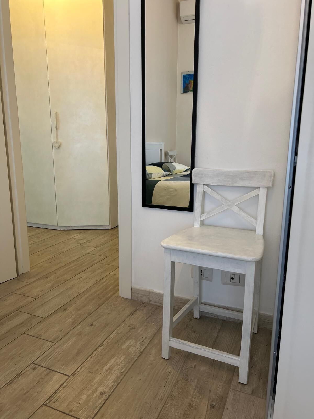 A white chair with a crisscross backrest in a room with wooden flooring and a white wardrobe.