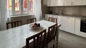 A modern kitchen with white cabinets, a dining table with chairs, and a window with curtains. - Casagrande Milan (Milano)