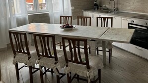 A modern kitchen with white cabinets, a dining table with chairs, and a large window with sheer curtains. - Casagrande Milan (Milano)
