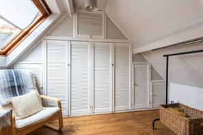 A room with a sloped ceiling, white shutters, a wooden floor, a wicker basket, and a striped cushion on a chair. - Cosy country cottage, a rural idyll near Dorking & Gatwick - 30 miles to London (Dorking)