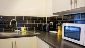 A kitchen with a sink, black tiled backsplash, a kettle, a microwave, and a knife block. - Praise Suite | Stylish Apartment • Parking • Wi-Fi (Barry)