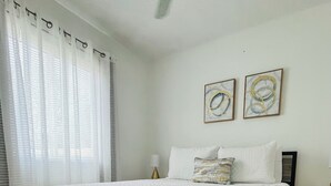 Ein Schlafzimmer mit einem Bett, Vorhängen, einem Nachttisch und zwei Wandbildern.