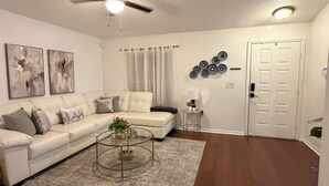 Ein Wohnzimmer mit einem weißen Sofa, einem Couchtisch, einem Deckenventilator und einer Tür.
