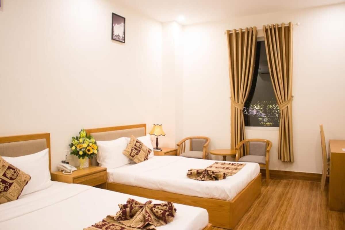 A hotel room with two beds, a nightstand with a lamp, a chair, a desk, and a window with curtains.