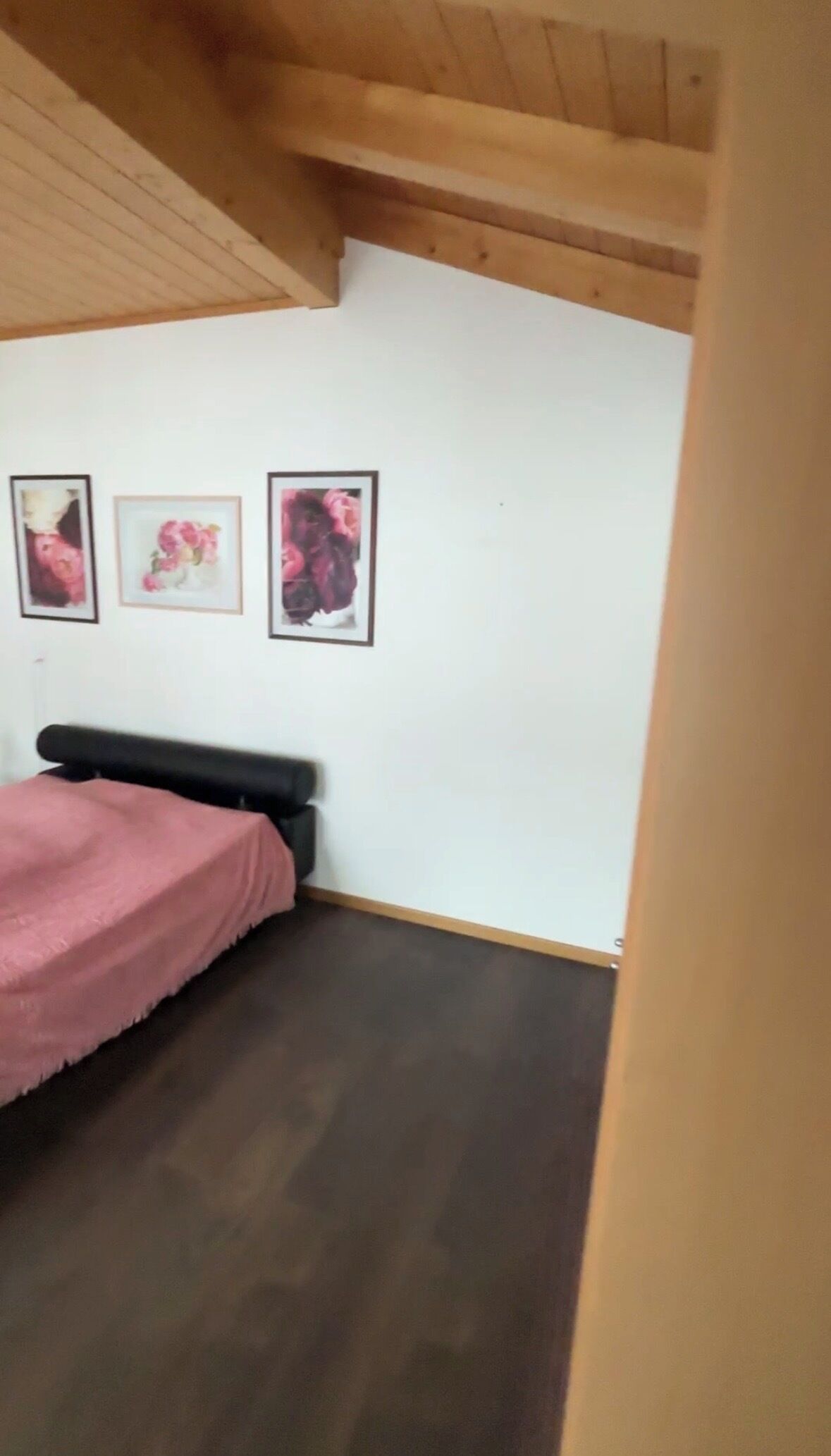 Ein Schlafzimmer mit einem Bett, einer Holzbalkendecke und drei gerahmten Bildern an der Wand.
