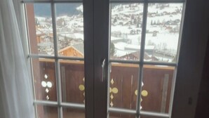Een kamer met een schuifdeur naar een balkon met uitzicht op besneeuwde bergen.