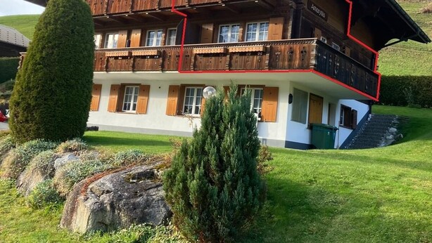 Een chalet met meerdere verdiepingen, houten balkons, een trap en een verzorgd gazon.