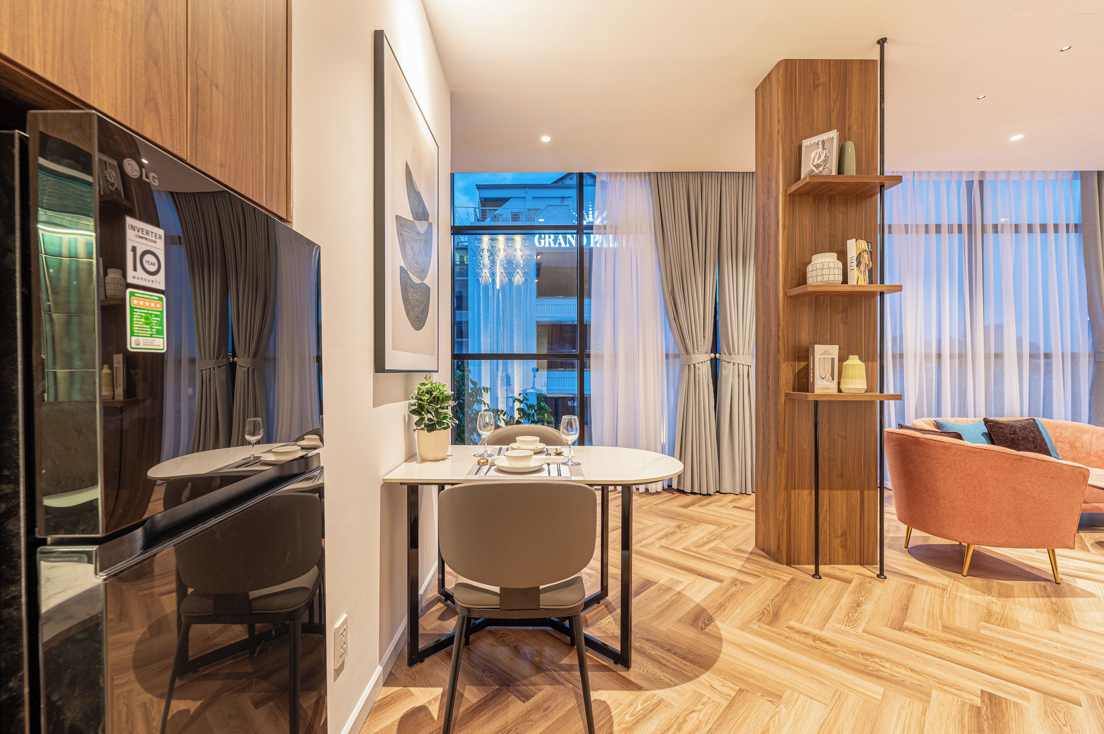 A modern hotel room with a dining area, a wooden floor, a sofa, and a view of the city.