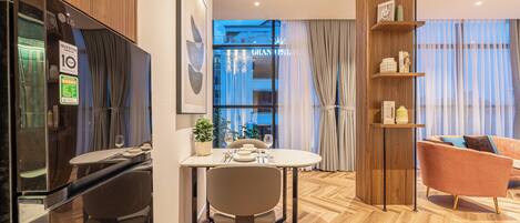 A modern hotel room with a dining area, a wooden floor, a sofa, and a view of the city.