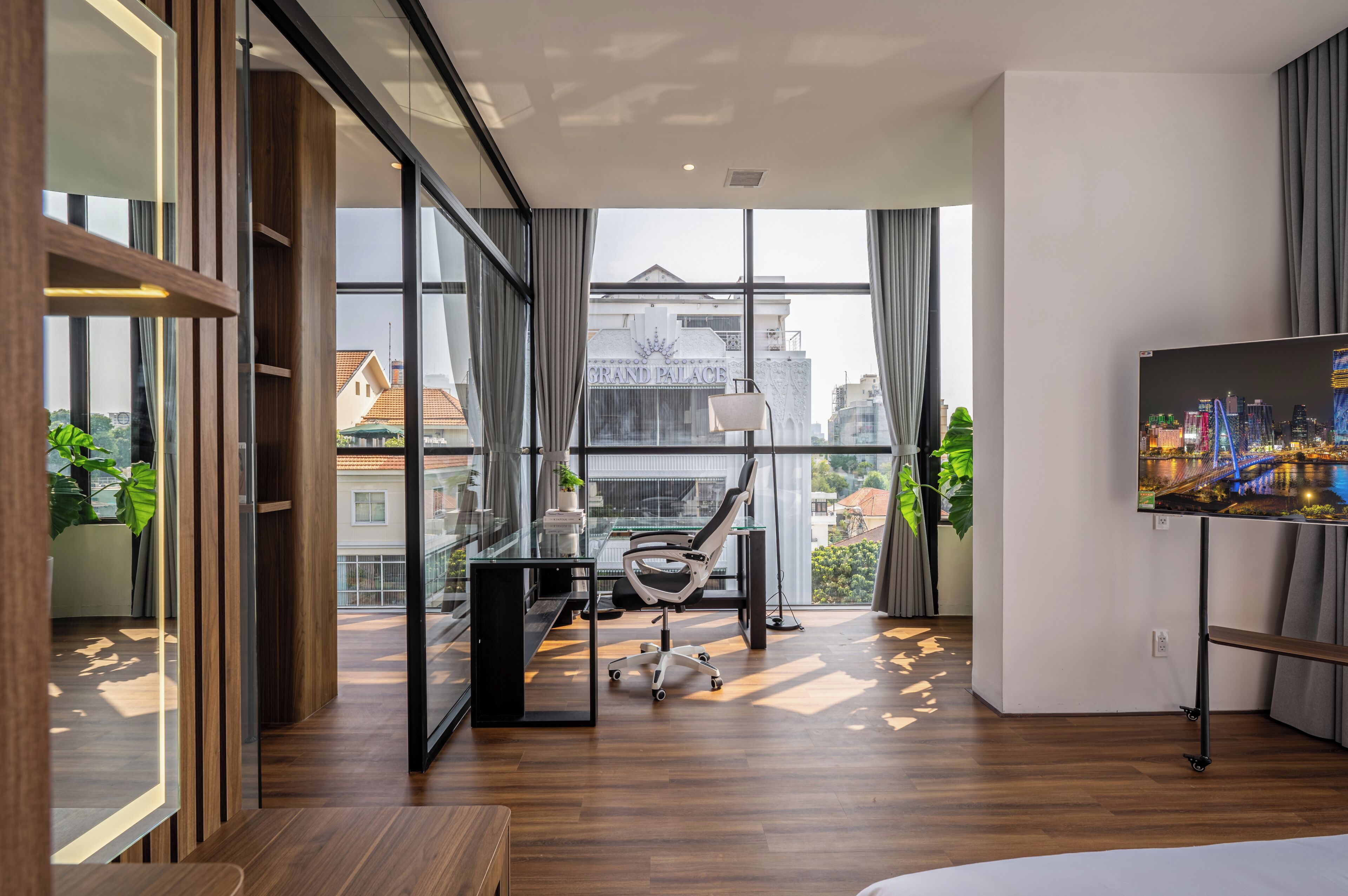 A modern office space with a large window, a desk, a chair, and a television.