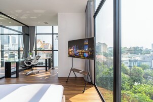 Habitación de hotel moderna con un televisor grande, un escritorio con silla, una cama y vistas a la ciudad.