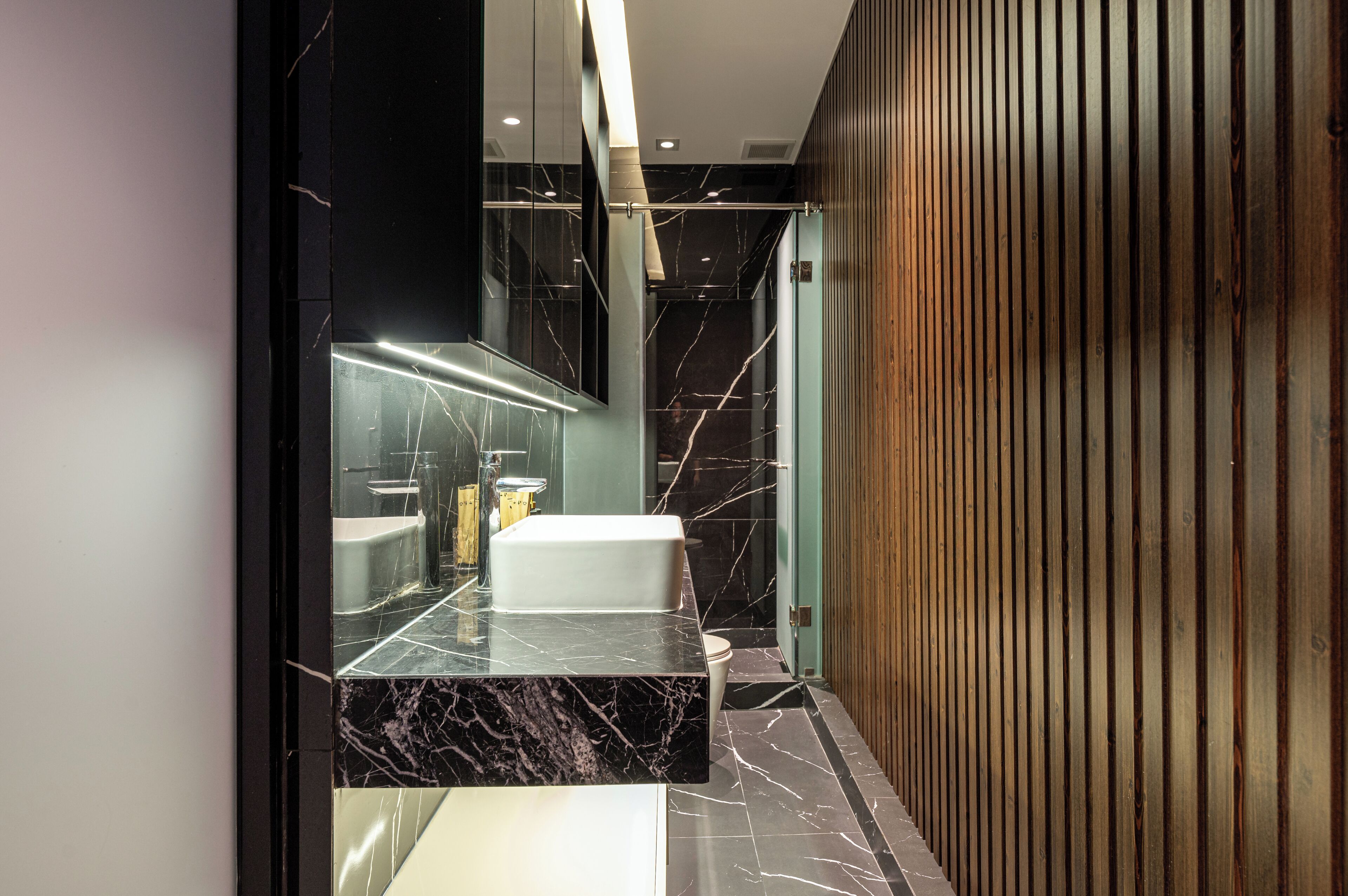 A modern bathroom with a marble countertop, a white sink, and a wooden panel wall.