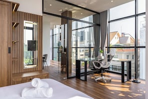 Habitación de hotel moderna con una cama grande, un escritorio de vidrio, una silla y vistas de la ciudad a través de amplias ventanas.