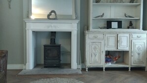 A room with a fireplace, a white cabinet with decorative items, and a round rug on the floor. - Cosy Romantic Cottage with Parking a short drive from the North Lakes & Pennines (Penrith)