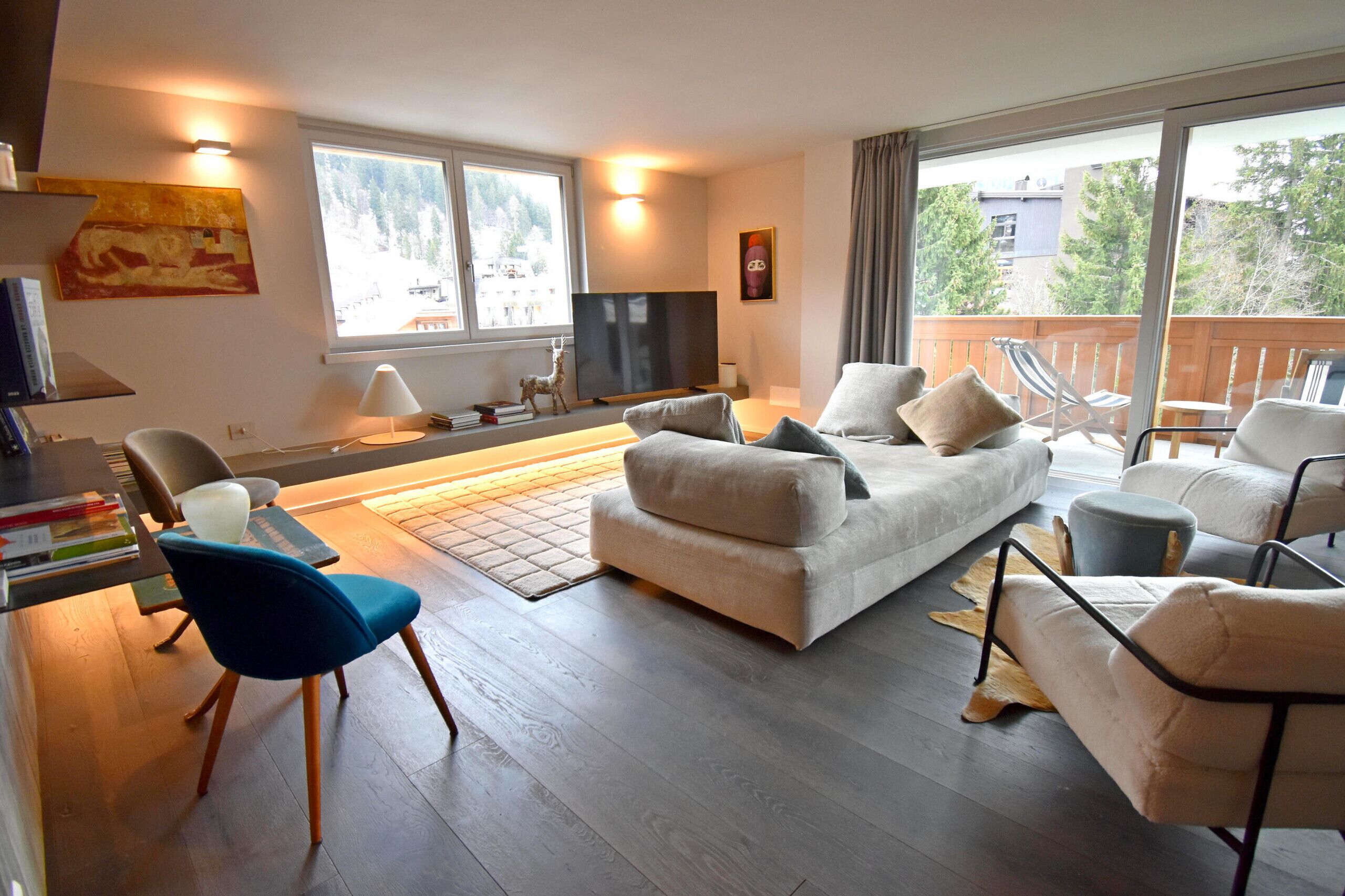 A modern living room with a sofa, chairs, a TV, and a balcony with a view.