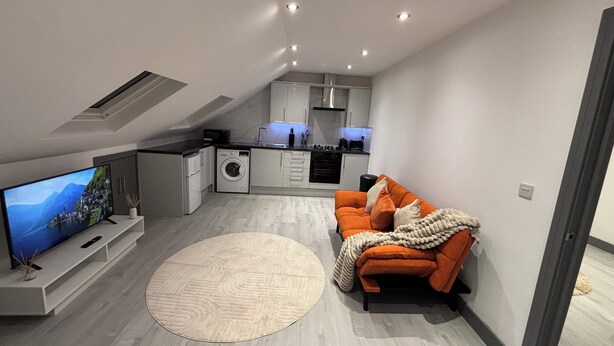 A compact living space with a kitchen, a sofa, a television, and a washing machine. - Stylish 1 Bedroom Apartment in East Croydon - Fast Link To Gatwick Airport (Croydon)