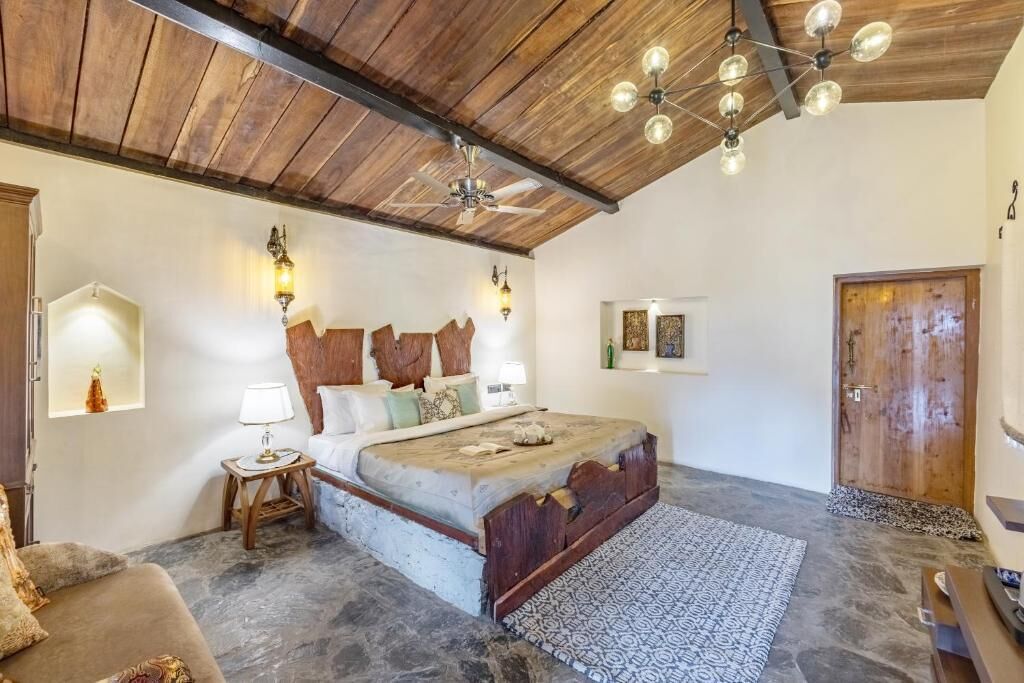 A bedroom with a wooden ceiling, a bed with a headboard made of wood, a nightstand with a lamp, and a patterned rug on the floor.