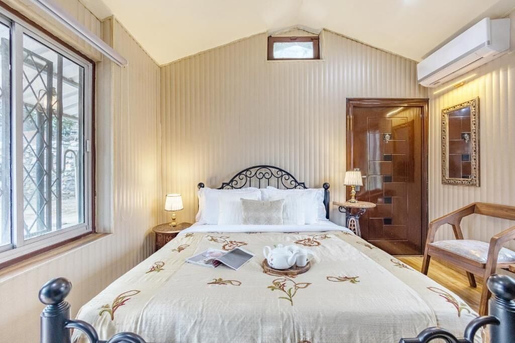 Un dormitorio con cama, mesita de noche, lámpara, silla, ventana y puerta.