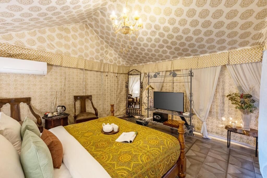 Habitación de hotel con techo estampado, cama con colcha amarilla, televisor sobre un mueble y un espejo.