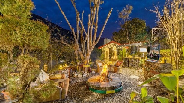 A cozy outdoor seating area with a fire pit, wicker furniture, and a small building with a red roof.