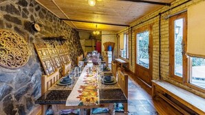 A long dining table with chairs, a chandelier, stone walls, and wooden beams.