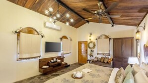 A bedroom with a bed, a TV, a wooden ceiling, and a ceiling fan.