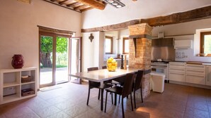Une cuisine avec une cheminée en pierre, une table à manger avec des chaises et une vue sur l’extérieur.