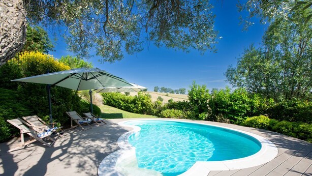 Une piscine à bordures courbes, entourée d’une terrasse avec des chaises longues et un parasol.