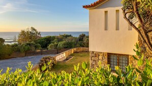 A coastal house with a stone wall, a garden, and a view of the sea.