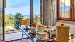 A dining area with a view of the ocean, a wooden table set with bowls, cups, and a wicker basket.