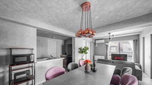 Una cocina moderna con microondas y cafetera sobre un carrito, una zona de comedor con mesa y sillas, y un espacio de sala de estar con sofá y televisor mostrando 'NETFLIX'.