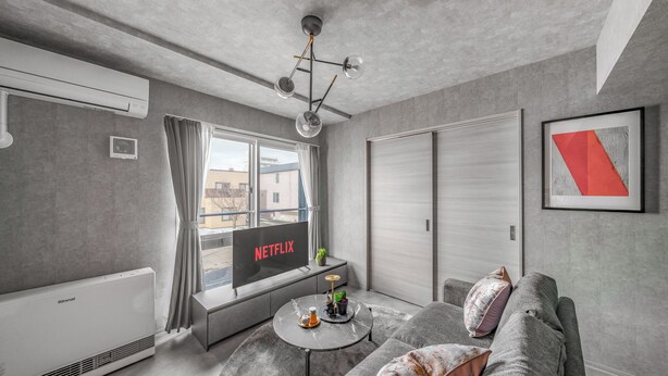 Una sala de estar moderna con un sofá gris, una mesa de centro, un televisor y un ventanal con cortinas.