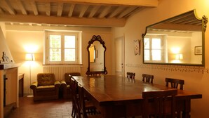 Une salle à manger avec une longue table en bois, six chaises, une cheminée et un miroir au mur.