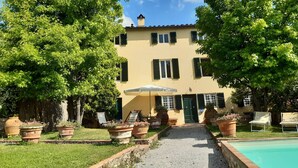 Un bâtiment à deux étages doté d’une piscine, entouré de plantes en pot et agrémenté de coins salon extérieurs.