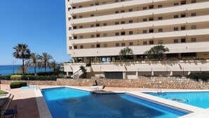 Ett hotell med flera våningar, en swimmingpool, palmer och utsikt över havet.