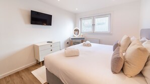 Ein Schlafzimmer mit Bett, Nachttisch, Schminktisch, Spiegel und einem an der Wand befestigten Fernseher.