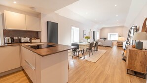 Eine moderne Küche mit einer zentralen Kochinsel, ein Essbereich mit Tisch und Stühlen sowie ein Wohnbereich mit Sofa und Fernseher.