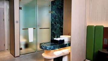 Une salle de bain moderne avec une douche à parois de verre, un lavabo en marbre et un banc avec des serviettes.
