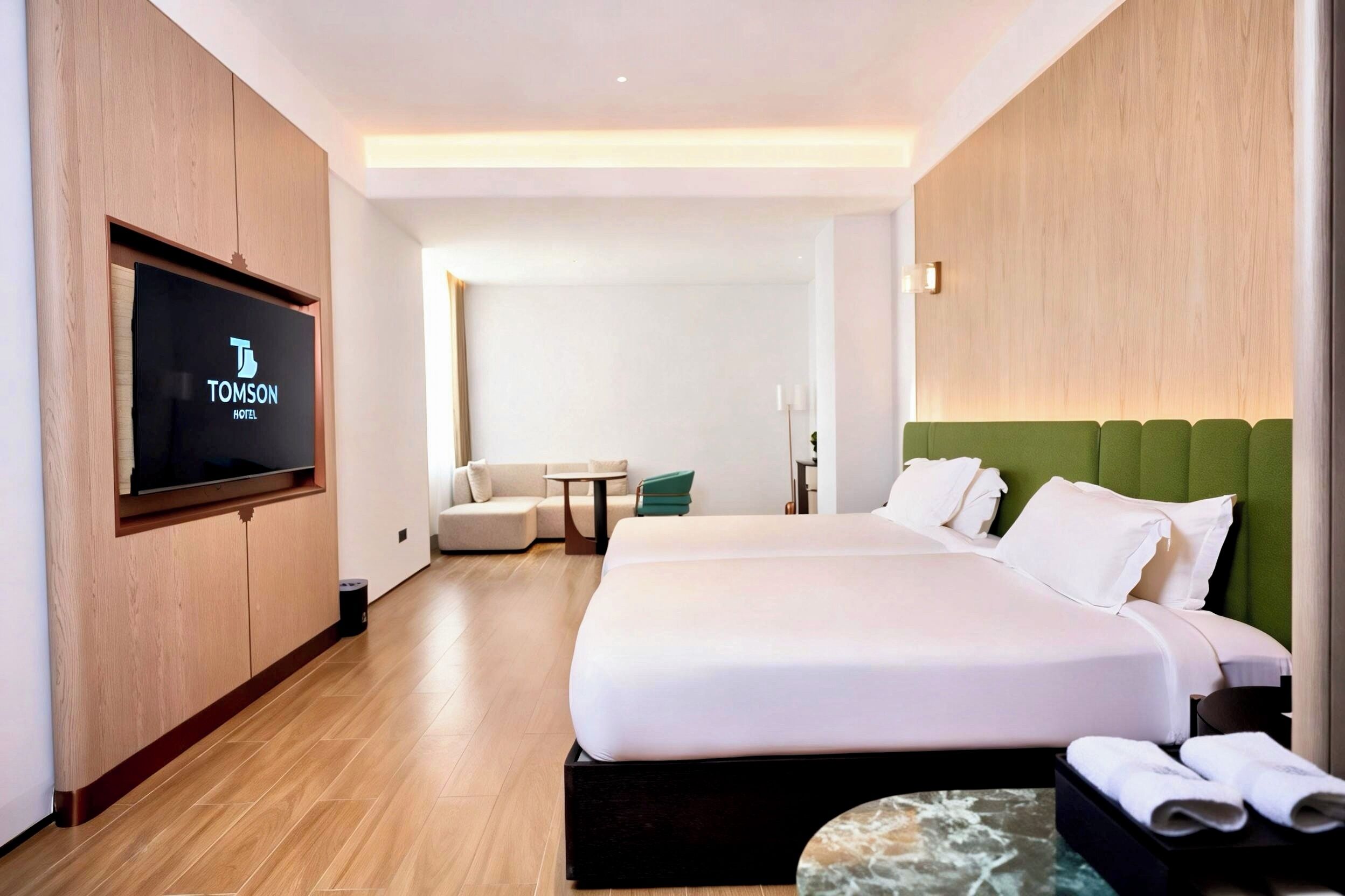 Quarto de hotel com uma cama grande, televisão fixada na parede, uma mesinha e um sofá.