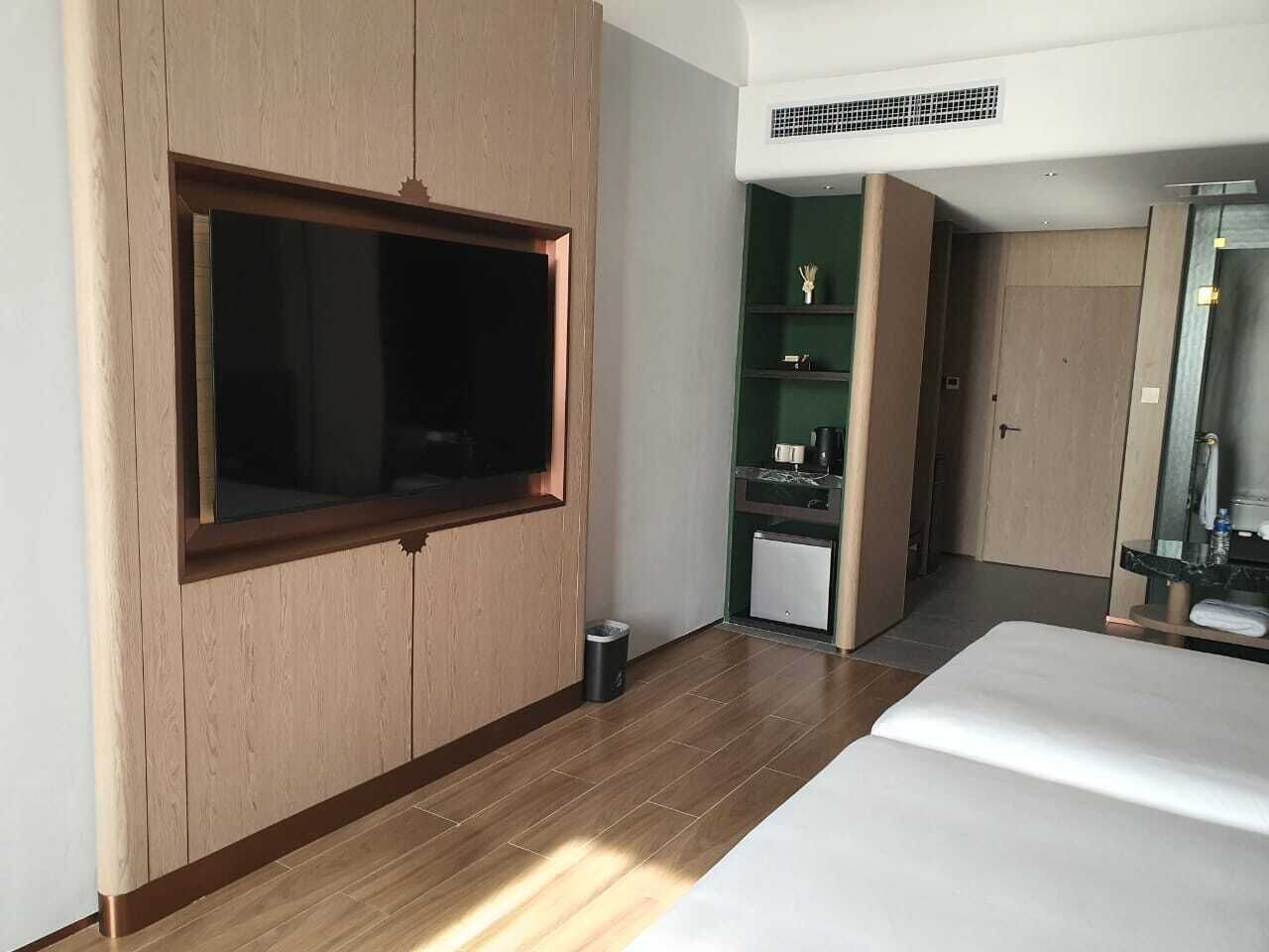 Ett modernt hotellrum med en stor säng, en inbyggd TV, ett litet pentry och ett badrum med spegel.